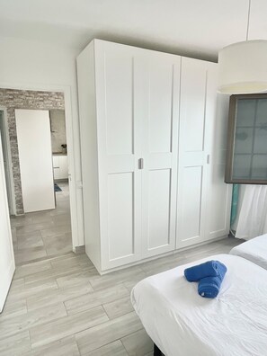 Ein Hotelzimmer mit großem Kleiderschrank, einem Bett mit weißer Bettwäsche und einem sichtbaren Badezimmer im Hintergrund.