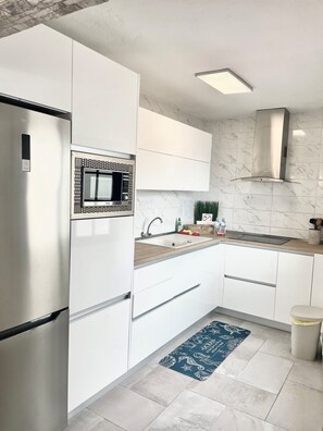 Eine moderne Küche mit weißen Schränken, einer eingebauten Mikrowelle, einer Edelstahl-Dunstabzugshaube und einer Holz Arbeitsplatte.