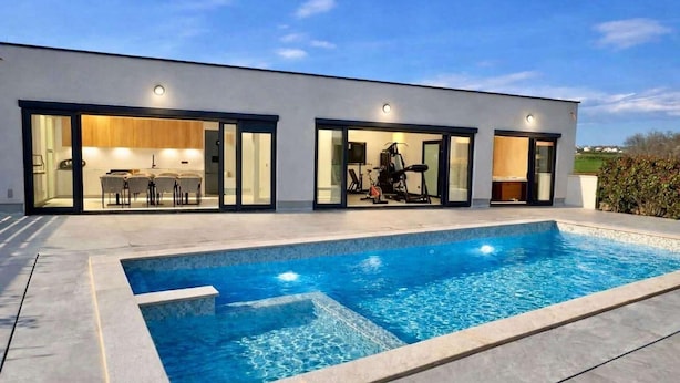 A modern house with a swimming pool, glass doors leading to a dining area, and exercise equipment visible through the doors. - 4-br Villa, Sleeps 16 With Hot Tub, Pool & Parking (Vrsar)