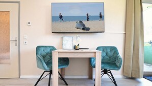 Ett rum med ett träbord, två turkosa stolar, en inramad bild av en strandvy och en flaska champagne.