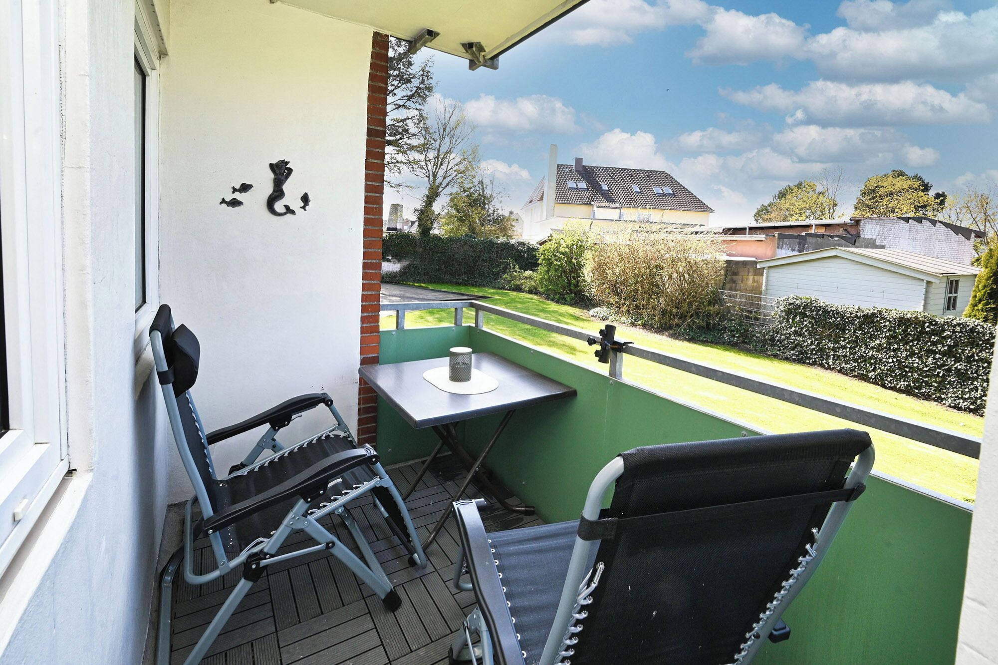 A balcony with two chairs, a small table, and a view of a residential area.