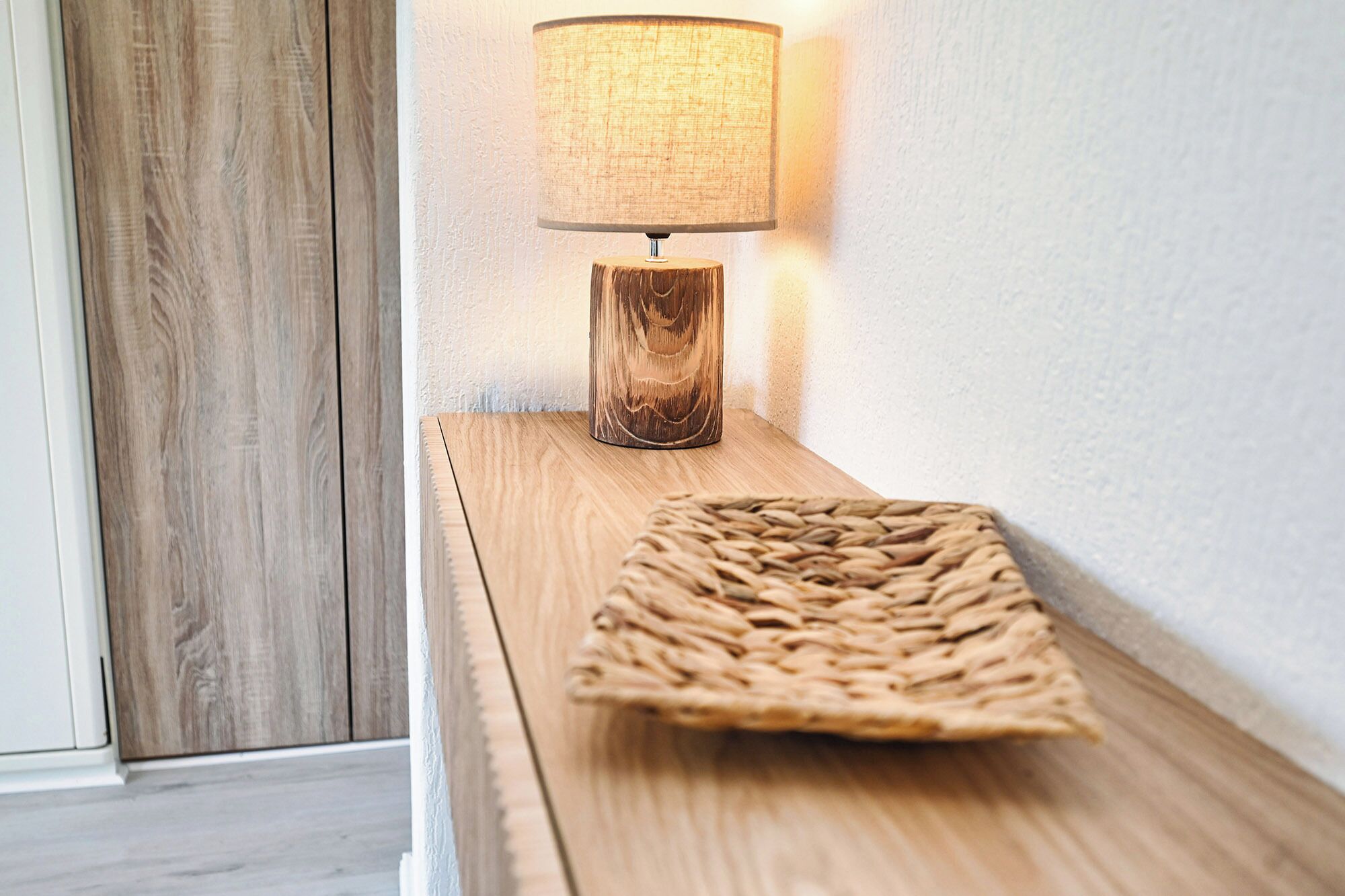 Une table de chevet en bois, sur laquelle est posée une nappe tressée, et une lampe avec un abat-jour texturé.