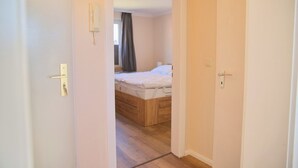 A bedroom with a wooden bed, a white bedside table, and a door with a keyhole. - Dünentraum 9 in Grömitz: 34 m² with a balcony, private parking, and Wi-Fi (Grömitz)