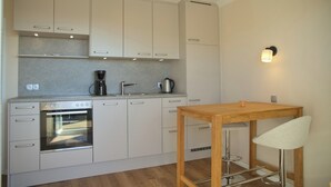 A modern kitchen with white cabinets, a built-in oven, a coffee maker, and a wooden table with a bar stool. - Dünentraum 9 in Grömitz: 34 m² with a balcony, private parking, and Wi-Fi (Grömitz)