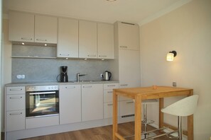 Eine moderne Küche mit weißen Schränken, einem eingebauten Backofen, einer Kaffeemaschine und einem Holztisch mit Barhocker.