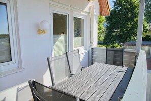 Eine Terrasse mit Tisch und Stühlen, ein Fenster mit Jalousien und eine weiße Wand.