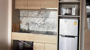A compact kitchen with a built-in microwave, a stainless steel refrigerator, a marble backsplash, and wooden cabinetry. - Coconut Suite Aonang (Krabi)