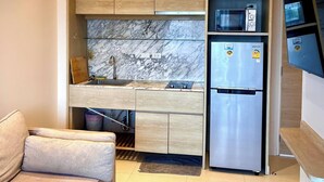 A compact kitchen with built-in appliances, a marble backsplash, and a sofa in the living area. - Coconut Suite Aonang (Krabi)