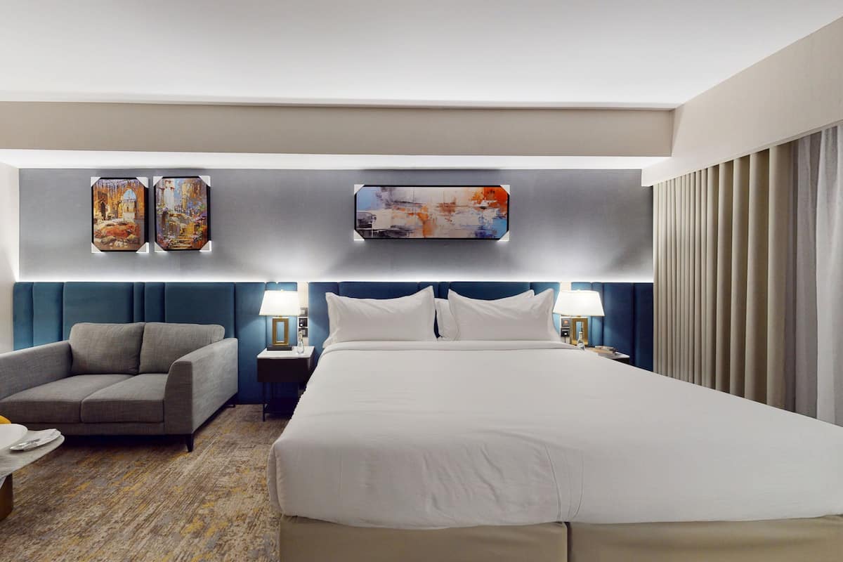 Quarto de hotel com uma cama grande, um sofá, uma escrivaninha e obras de arte nas paredes.