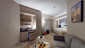 Habitación de hotel con cama, sofá, mesa de comedor con desayuno, minibar y un amplio ventanal.