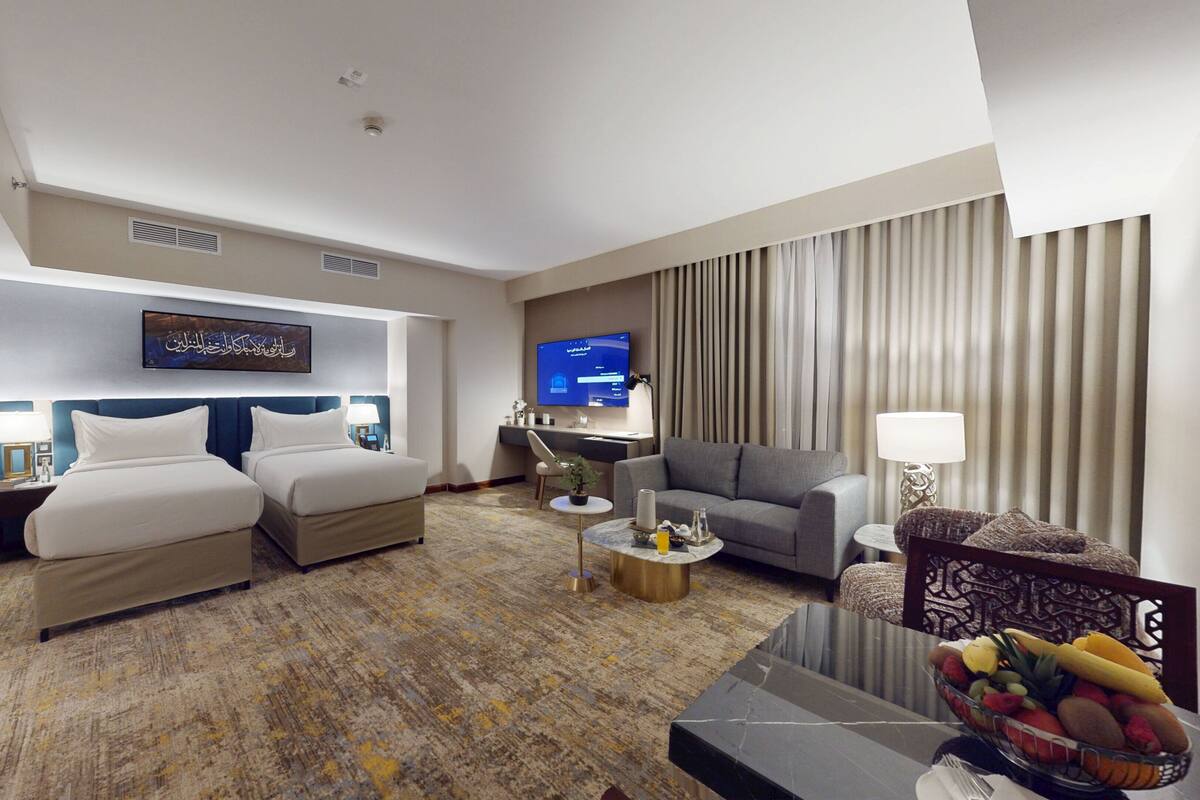 Quarto de hotel com cama, sofá, televisão e mesa de centro.