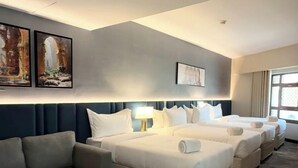 Habitación de hotel con sofá, dos camas, una mesita redonda y obras de arte en las paredes.