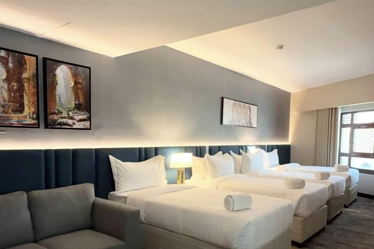 Quarto de hotel com sofá, duas camas, mesa de centro redonda e obras de arte nas paredes.