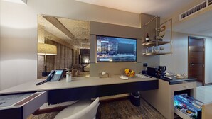 Habitación de hotel con escritorio, teléfono, televisor, minibar y cama.