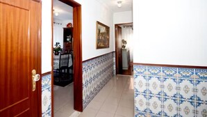 Un corridoio con pavimento piastrellato, una porta in legno e una sala da pranzo con sedie e tavolo.