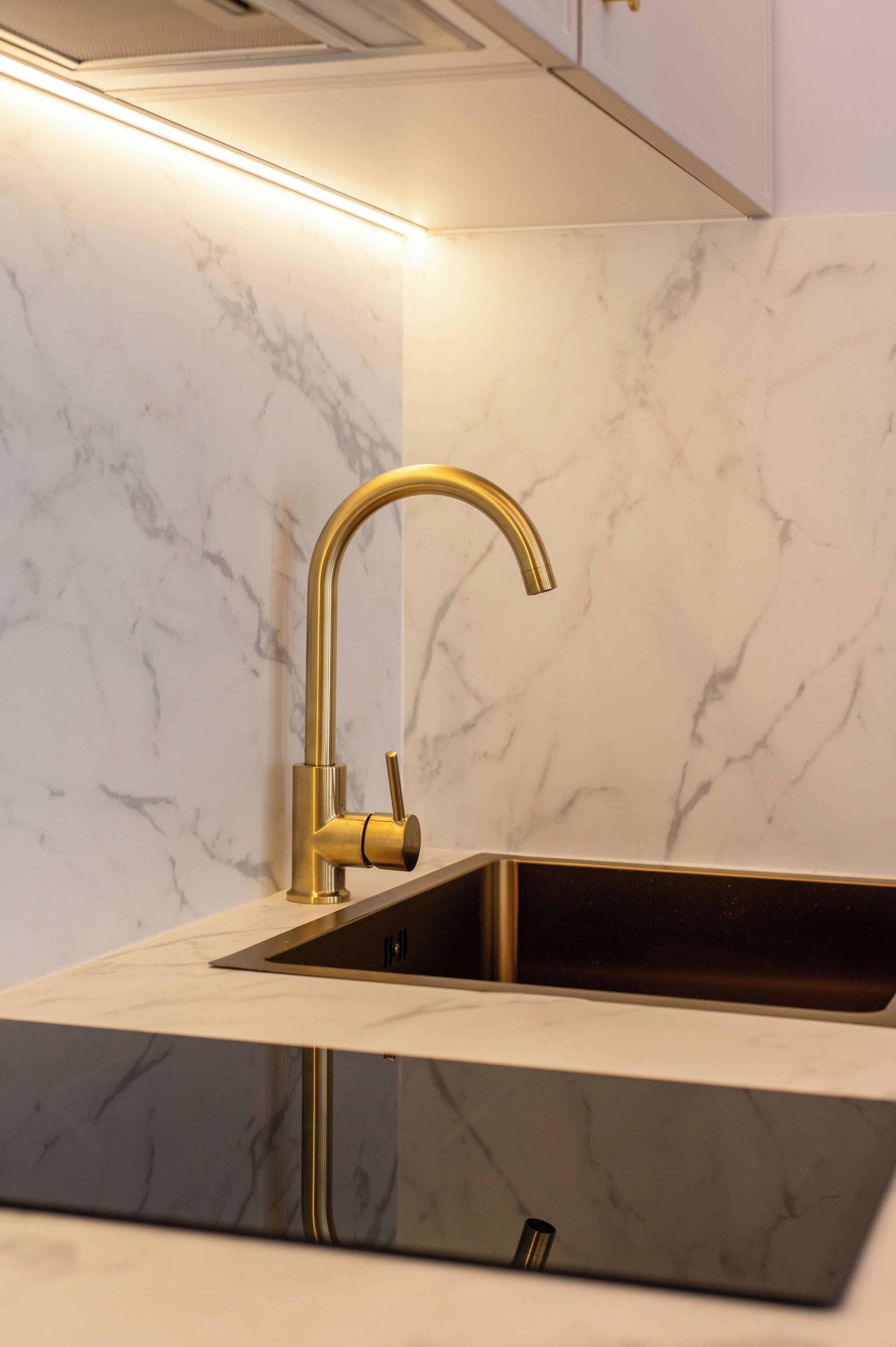Een keuken met een gouden kraan, marmeren aanrecht en een zwarte spoelbak.