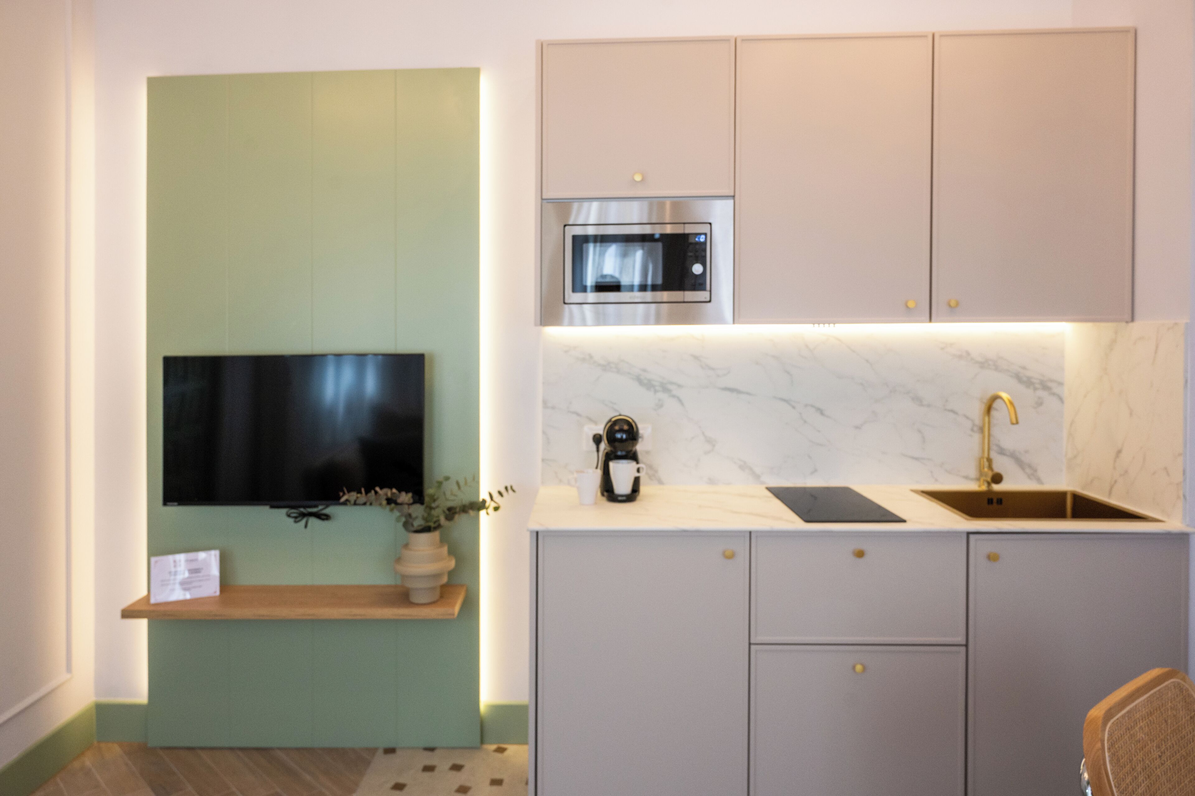 A modern kitchen with a built-in microwave, a sink, and a flat-screen TV mounted on the wall.