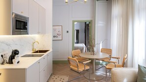 A modern kitchen with a built-in oven, a coffee machine, and a dining area with a round table and wicker chairs. - 4Duques Apartments (Cáceres)