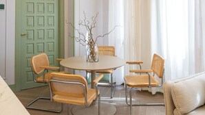 A dining area with a round table, wicker chairs, a vase with branches, a green door, and a white curtain. - 4Duques Apartments (Cáceres)