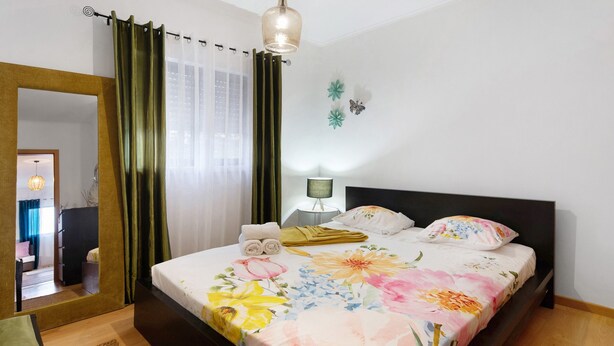 Ein Schlafzimmer mit Bett, Nachttisch, Lampe, Spiegel und Blick auf einen Flur.