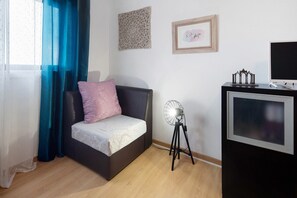 Ein Schlafzimmer mit einem Bett, einem Standventilator, einem Fernseher und einer Wanddekoration.