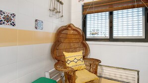 Ein Korbstuhl mit gemustertem Kissen, ein Heizkörper und dekorative Fliesen an der Wand.