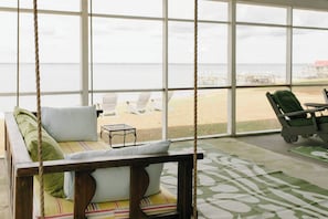 Una habitación con una silla colgante, vistas a la playa y una mesa con sillas.