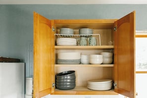 A kitchen cabinet with multiple shelves holding plates, bowls, and a kettle.