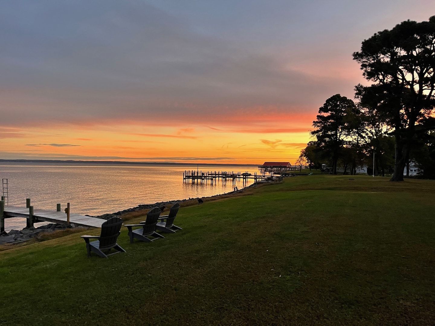 A lakeside view with a dock, chairs, and a grassy area.