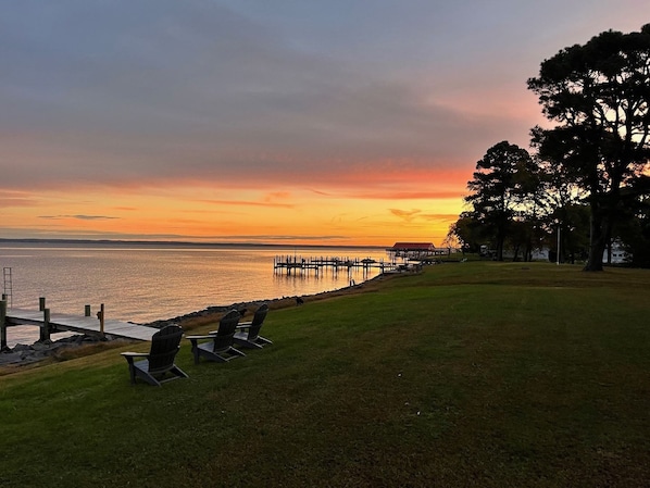 A lakeside view with a dock, chairs, and a grassy area.