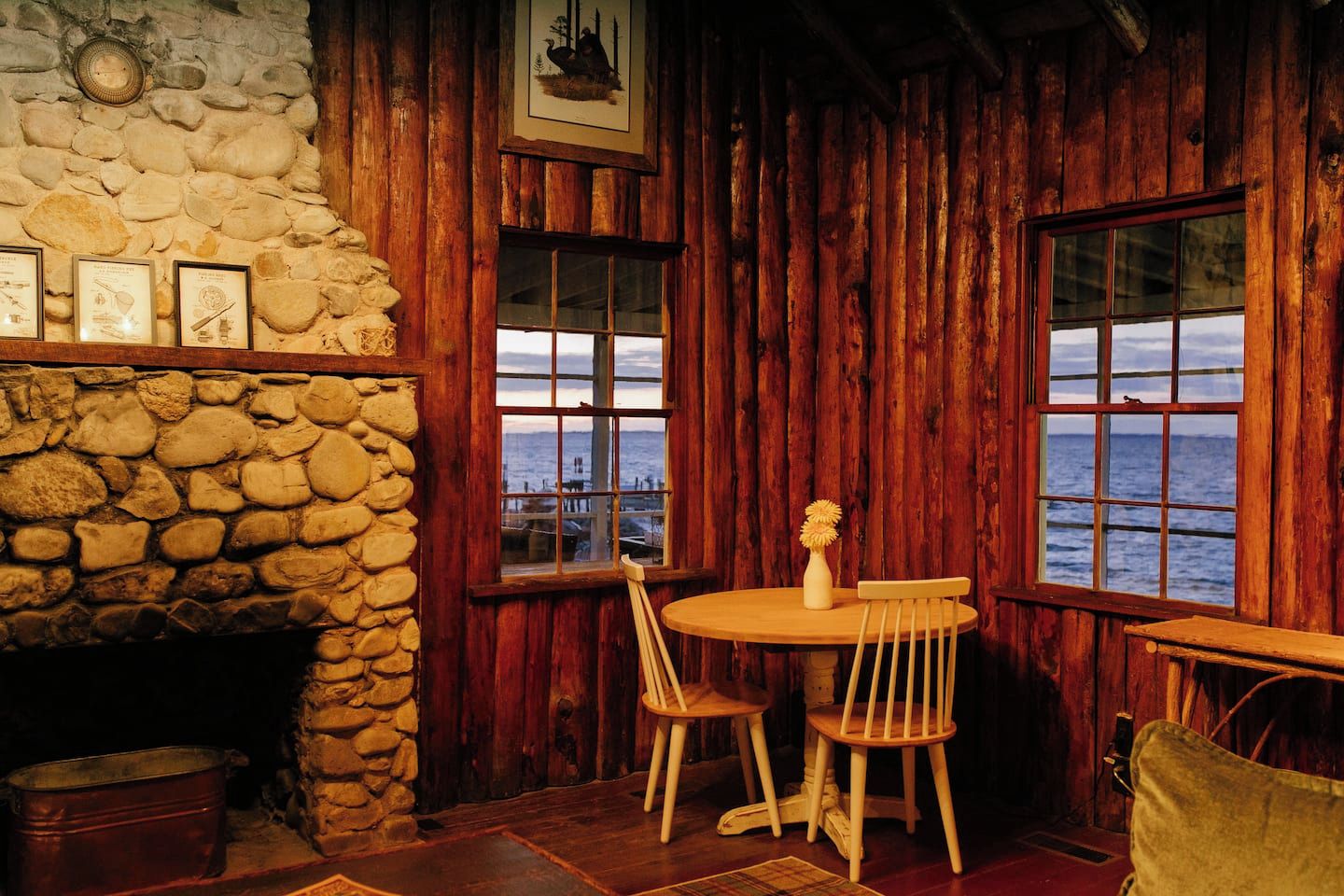 A rustic interior with a stone fireplace, wooden walls, and a table with chairs.