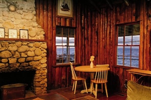 Un interior rústico con chimenea de piedra, paredes de madera y una mesa con sillas.