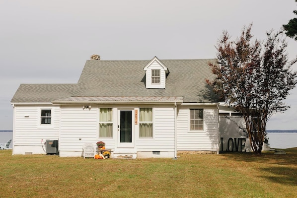 A white two-story house with a grey roof, a chimney, and a number '1074' on the door.