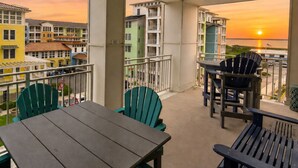 En balkon med bord og stole, der udover et solnedgang og bygninger.