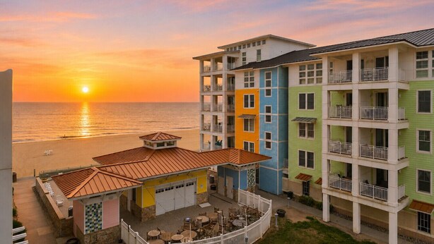 Et hotel med flere etager, altaner, poolområde og havudsigt i solnedgang.