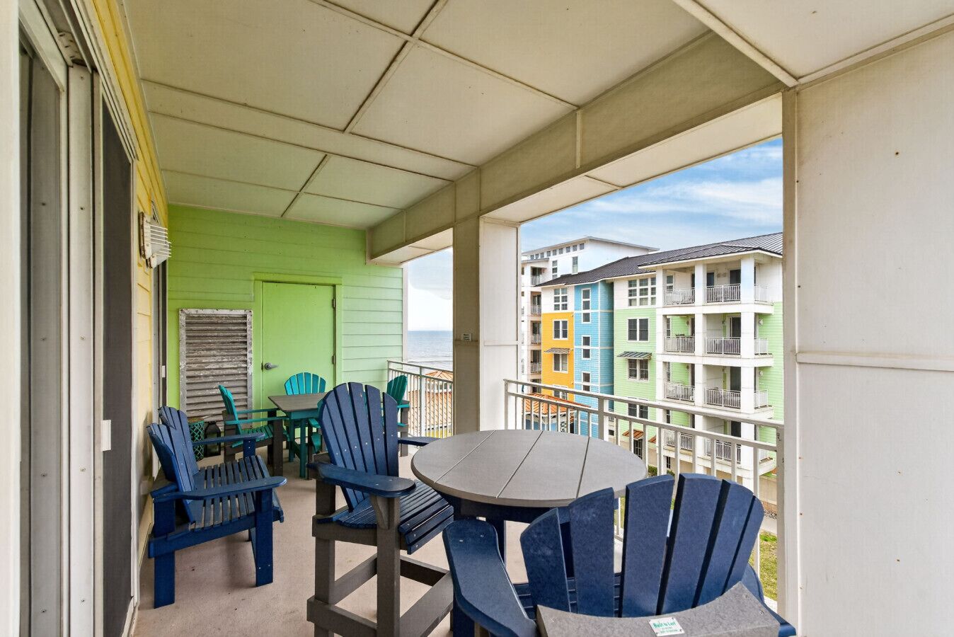 Un balcon avec une table et des chaises, une porte verte et une vue sur des bâtiments aux couleurs vives.