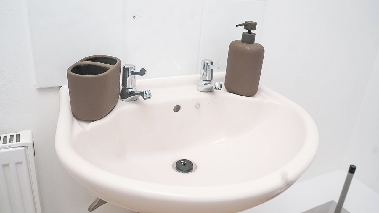 A white bathroom sink with two soap dispensers, a mirror, and a toilet paper holder.