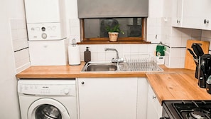 A compact kitchen with a washing machine, a sink with a dish rack, a window with a plant, and a stove. - Entire rental unit in Medway, United Kingdom - A comfort Zone (Gillingham)