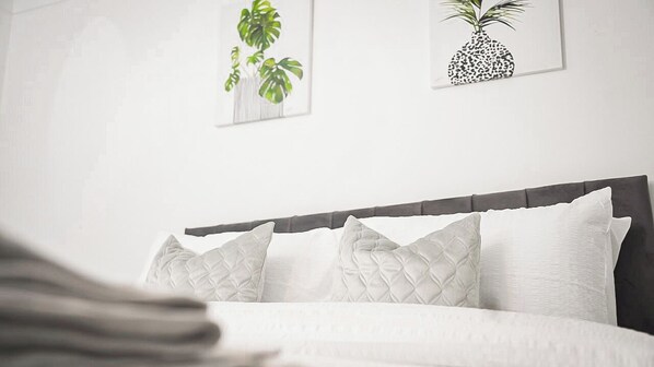 A bed with white bedding and a dark headboard, framed by two wall-mounted plant illustrations. - Entire rental unit in Medway, United Kingdom - A comfort Zone (Gillingham)