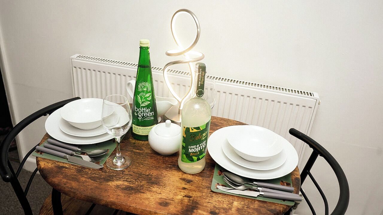 A dining table set with plates, cutlery, and bottles, with a radiator in the background.