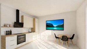 Een moderne keuken met een ingebouwde oven, een eethoek met een tafel en stoelen, en een tv aan de muur waarop een berglandschap wordt getoond.
