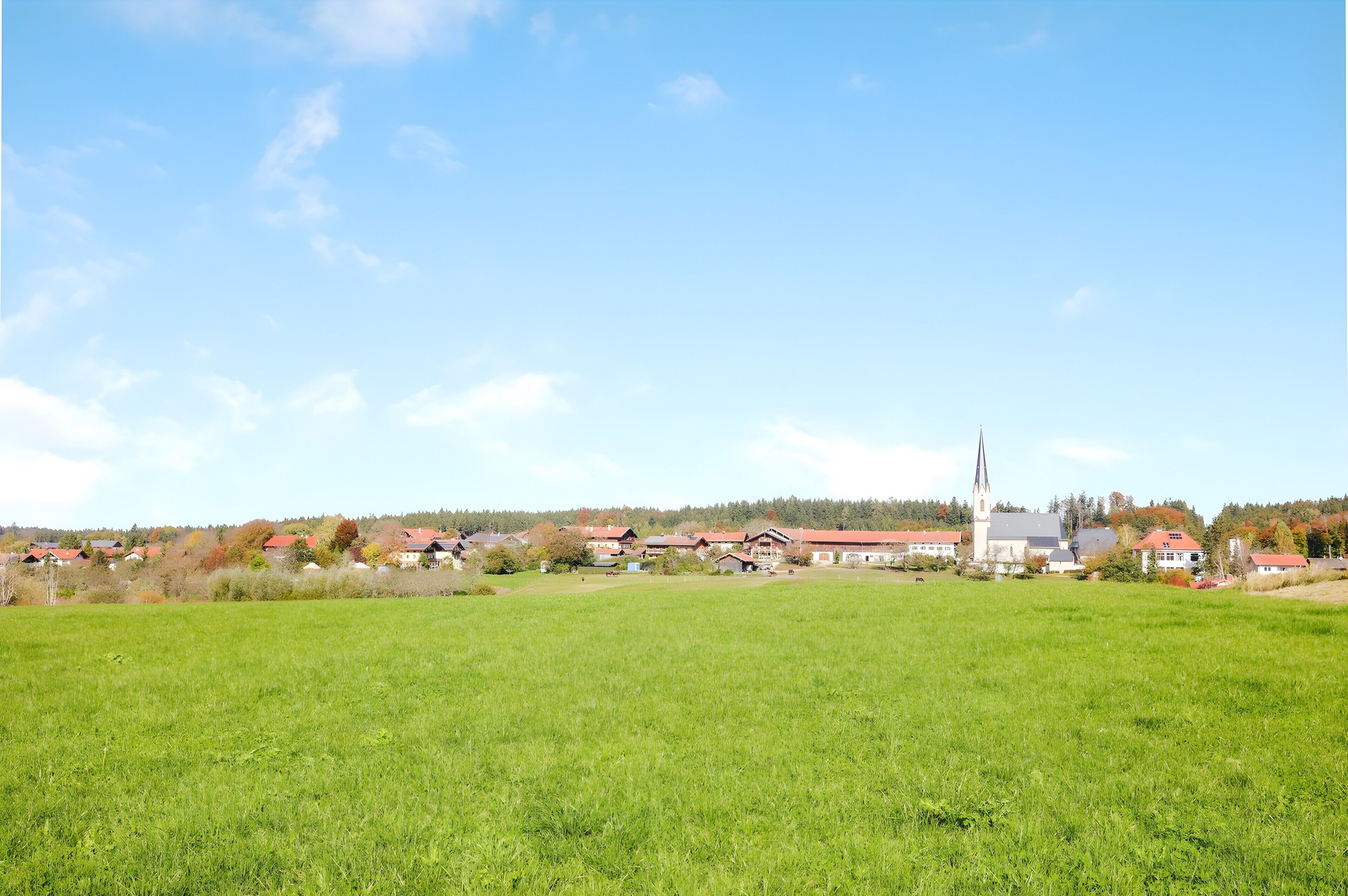 A rural landscape with a church, houses, and open fields.