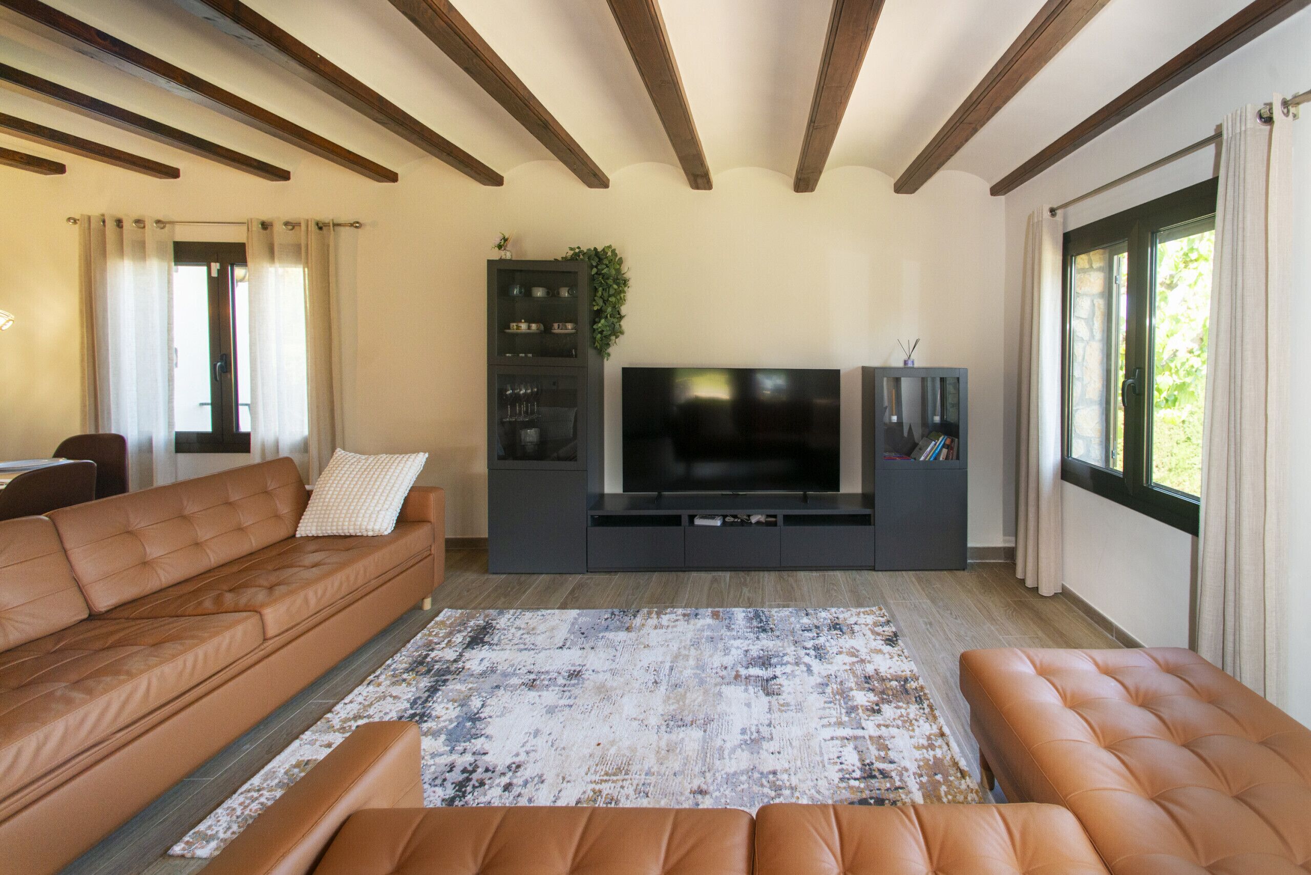 A living room with a sofa, ottoman, entertainment unit, and a large flat-screen TV.