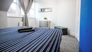 Quarto com cama, cômoda, espelho e janela com cortinas.