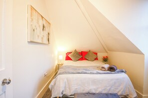 Ein Schlafzimmer mit einem Bett, Kissen, einer Nachttischlampe und einem Bild an der Wand.