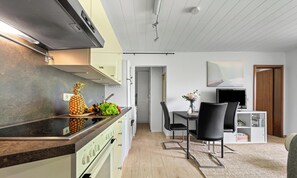 A modern kitchen with a built-in stove, a dining area with a table and chairs, and a living space with a TV and a bookshelf. - "Ankerplatz" Vacation Apartment in Büsum: With Terrace, Wi-Fi, Family-Friendly, (Büsum)
