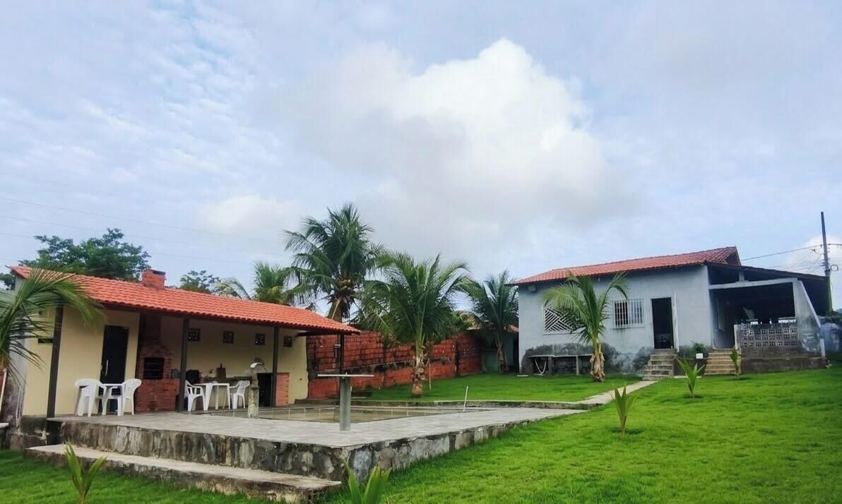A house with a red-tiled roof, a patio with chairs, and a grassy yard with palm trees.