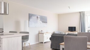 A modern living room with a dining area, a television, and a painting of a lighthouse. - Vacation apartment Hafenperle (Laboe)
