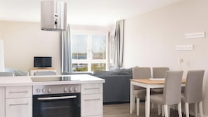 A modern kitchen with a built-in oven, a dining area with a table and chairs, a sofa, and a television on a side table. - Vacation apartment Hafenperle (Laboe)