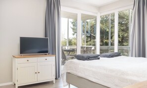 Ein Schlafzimmer mit einem Bett, einem Fernseher auf einer Kommode und einem Balkon mit Blick auf Bäume.